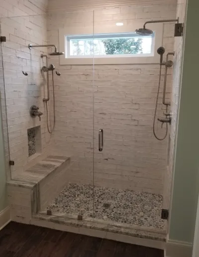 A bathroom with a glass shower door and a bench.