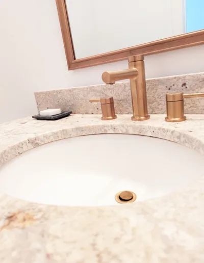 A bathroom sink with a gold faucet and mirror.