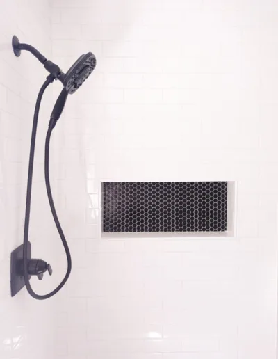 A black shower head with a white tiled shower.